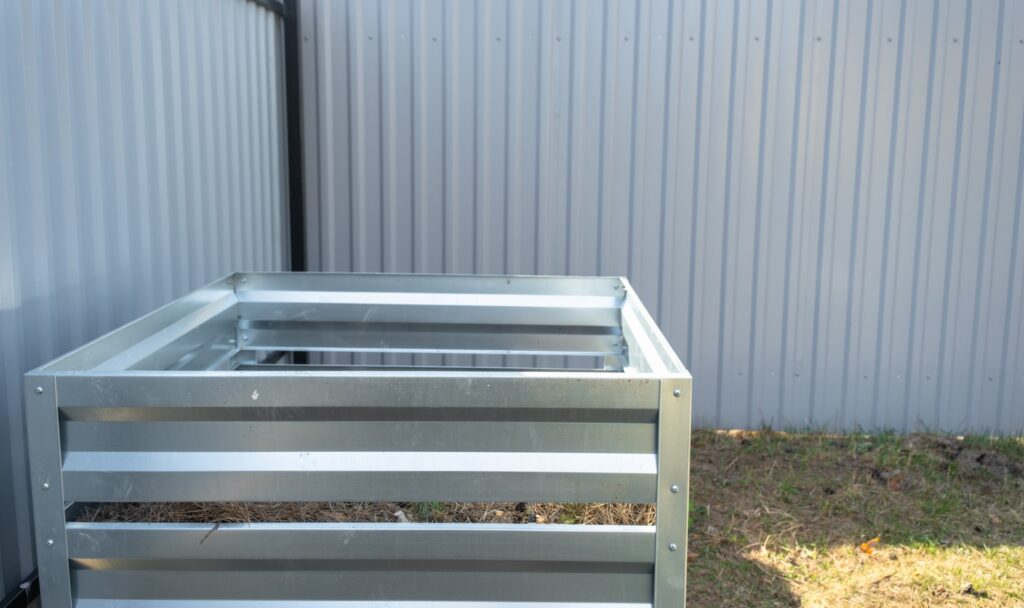 Composter made of metal for organic waste near the fence on suburban area. Compost box for eco-frien